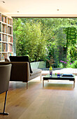 Chaise longue and bookcase at full length window to back garden in London home, England, UK