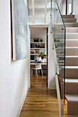 Glass staircase partition allowing natural light into narrow hallway of London home, England, UK