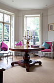 Round mahogany pedestal table with bright pink chair and cushions in Georgian style room