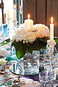 Glaswaren und weiße Rosen mit brennenden Kerzen auf einem Esstisch in einem Haus in den Cotswolds, Großbritannien