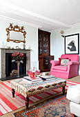 Rosa gepolsterter Sessel im Wohnzimmer mit antikem Glasschrank, Haus in East Sussex, England, UK