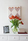 Vase of tulips and heart shaped artwork on white painted sideboard London UK