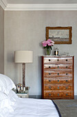 Wooden chest of drawers and cream bedside lamp in contemporary London townhouse, UK