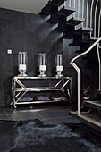 Three hurricane lamps on metallic console under open tread staircase in entrance hall of contemporary London townhouse, UK