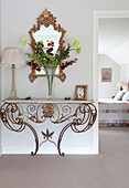 Cut flowers on metalworked console with gilt mirror in Sussex home UK