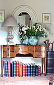 Hardbacked reference books under sideboard with cut tulips in hallway of Sussex farmhouse, UK