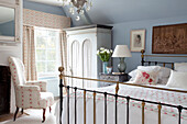 Co-ordinating fabrics in light blue bedroom with brass bed in Sussex farmhouse, UK