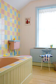 Panelled bath in room with multicoloured pastel tiles and blue painted radiator, Rye home, East Sussex, England, UK
