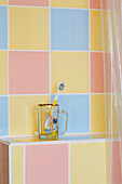 Toothbrush in glass cup with multicoloured pastel tiles in bathroom of Rye home, East Sussex, England, UK