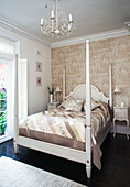 White painted for postered bed in bedroom with neutral floral patterned wallpaper, Surrey home, England, UK