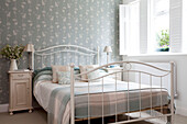 Light blue tartan blanket on white metal bed with floral wallpaper in Surrey home, England, UK