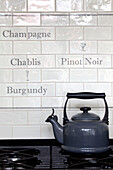 Grey kettle on gas hob with french lettering white tiled splashback in kitchen of Surrey home, England, UK