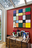 Colourful modern artwork and wooden chest with books in conservatory extension of London home, England, UK
