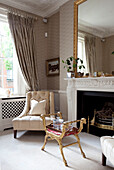 Cream armchair and large gilded mirror in living room of contemporary London townhouse, England, UK