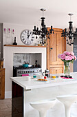 Matching chandeliers above breakfast bar in contemporary kitchen with clock above range oven in London home, UK
