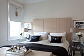 Marineblaue Kissen auf einem Doppelbett in einem modernen Schlafzimmer mit verspiegelten Beistelltischen in einem Haus in London, Vereinigtes Königreich