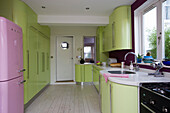Lime green retro styled kitchen with pink upright fridge in East Sussex home, England, UK
