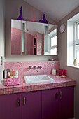 Mirrored cabinet above pink tiled wash basin in retro styled East Sussex home, England, UK