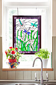 Stained glass window detail above sink with houseplants in London townhouse, England, UK