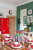 Bright orange upright fridge in green kitchen with set table in London townhouse, England, UK