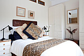 Gemusterte Kissen auf einem Bett mit geschnitztem Kopfteil in einem weißen Schlafzimmer in einem Londoner Stadthaus, England, UK