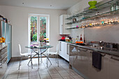 Glass table in contemporary London kitchen with fairlights and variety of cupboard units, UK