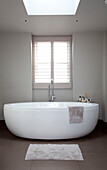 Freestanding contemporary white ceramic bath at window of London home, UK