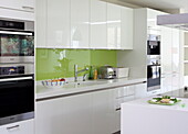 White fitted kitchen with green splashback and integral appliances in contemporary London home, England, UK