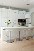 Bar stools at breakfast bar in white fitted kitchen of contemporary London home, UK