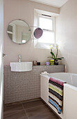 Circular mirrors above washbasin with sunlit window in contemporary bathroom of London home, UK