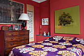 Holzkommode und Kunstwerk mit lilafarbenem Bettbezug in einem Haus in London, England UK