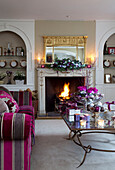 Striped vibrant pink sofa in living room of Surrey farmhouse with lit fire, England, UK