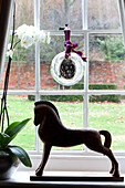 Glass bauble at window of Surrey farmhouse with orchid and horse statue, England, UK