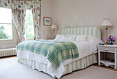 Green tartan blanket on double bed with striped headboard and valence in Sussex country house, England, UK