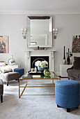 Glass topped coffee table and mirror with blue footstools in living room of London apartment, UK