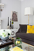 Yellow cushion and standard lamp with vases on coffee table in living room of London apartment, UK