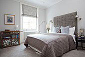 Neutral quilted bedcover with antique bookcase in London apartment, UK