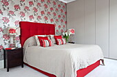 Blumentapete hinter rotem Kopfteil mit Knöpfen im modernen Schlafzimmer eines Londoner Stadthauses, England, UK