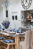 Nautical themed dining rom with table set in blue and white, portholes in door and large clock on wall and wine glass chandelier, Dulwich home, London, UK