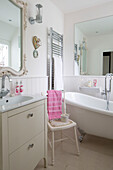 Pink towel on chair beside freestanding claw-foot bath in Dulwich home, London, UK