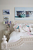 Kunstwerk über geblümten Kissen auf weiß gestrichenem Bett in einem Haus in Dulwich London UK