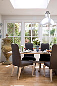 Dining table and chairs under chrome pendant light in conservatory of historic Sussex country home England UK