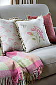Assorted cushions with pink checked blanket on sofa in Sussex Downs home England UK