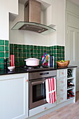 Casserole dish on gas hob in kitchen with green tiled splashback in London home, England, UK