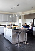 Chrome barstools at light grey kitchen island with glass orb shades in Kent home, England, UK