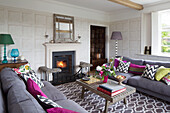 Befeuerter Kaminofen mit gemustertem Teppich und verschiedenen Kissen in einem Wohnzimmer in Herefordshire, England, Vereinigtes Königreich