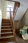 Green wicker chair in wooden staircase with arched window in Herefordshire home, England, UK