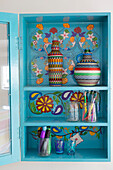 Hand woven bottle covers in painted wall-mounted cabinet in Herefordshire home, England, UK