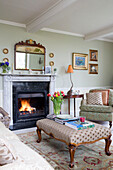 Cut tulips on ottoman with lit fire in living room of Burwash home East Sussex England UK