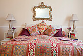 Ornate mirror above colourful quilted bed with matching lamps in West Sussex home, England, UK